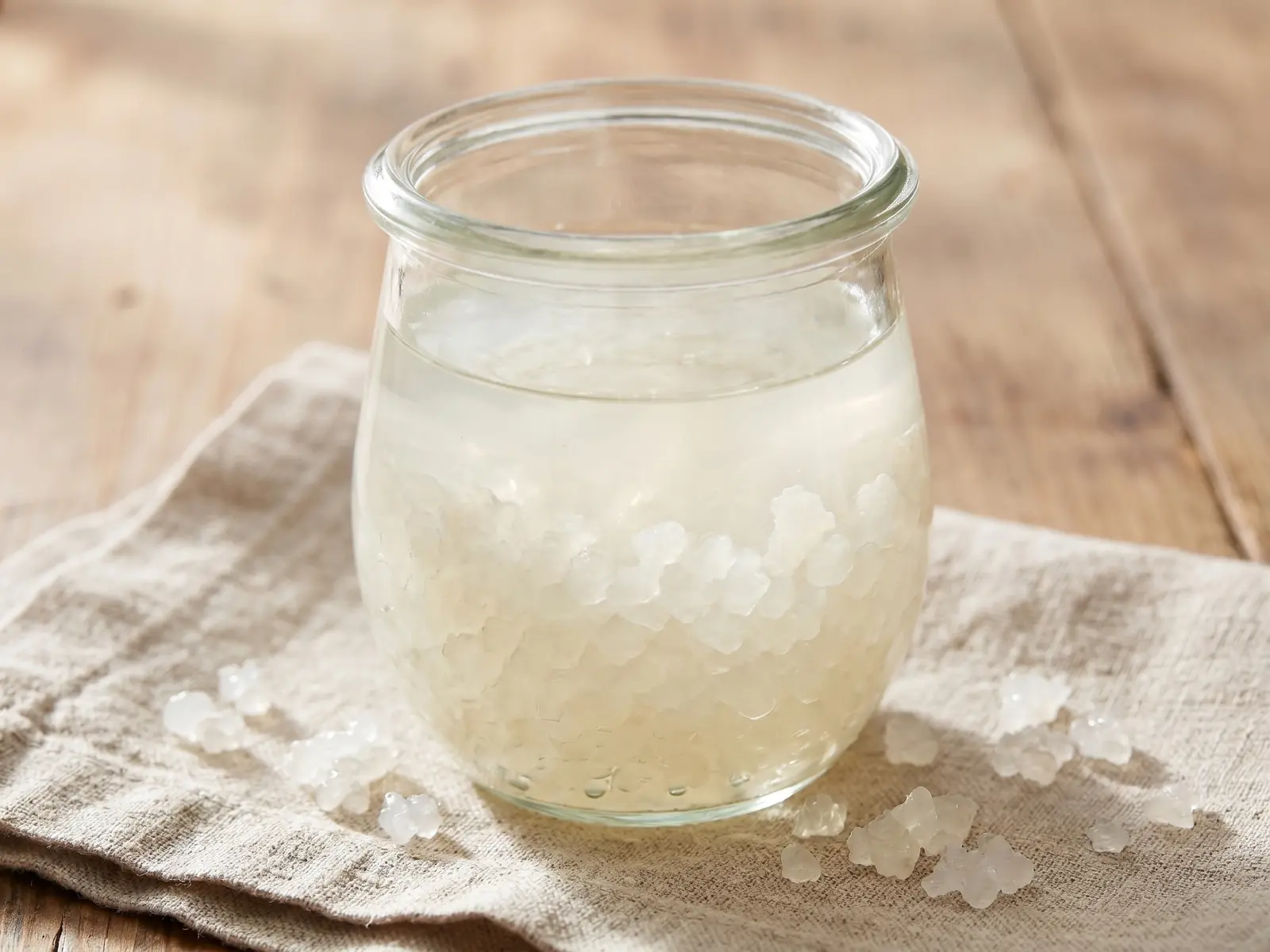 tibicos de agua Frasco limpo com kefir de água sobre linho cru, com grãos translúcidos em repouso no líquido.